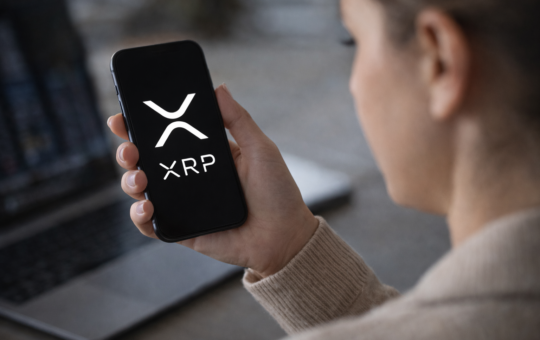 Person holding a smartphone displaying the XRP cryptocurrency logo while checking digital asset markets.